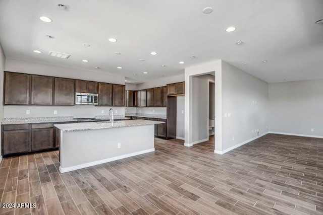 kitchen featuring light stone countertops, dark brown cabinetry, light wood-type flooring, and a kitchen island with sink