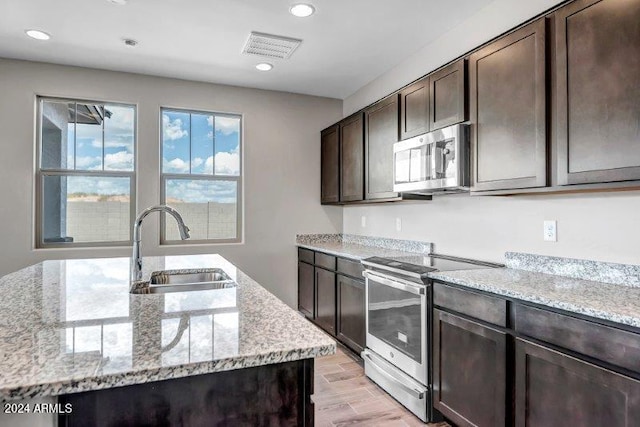 kitchen featuring appliances with stainless steel finishes, light wood-type flooring, light stone counters, dark brown cabinetry, and sink