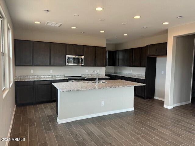 kitchen with stove, light stone counters, dark wood-type flooring, sink, and a center island with sink