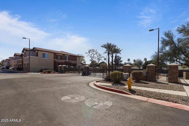 view of road featuring sidewalks, curbs, a residential view, a gate, and street lighting