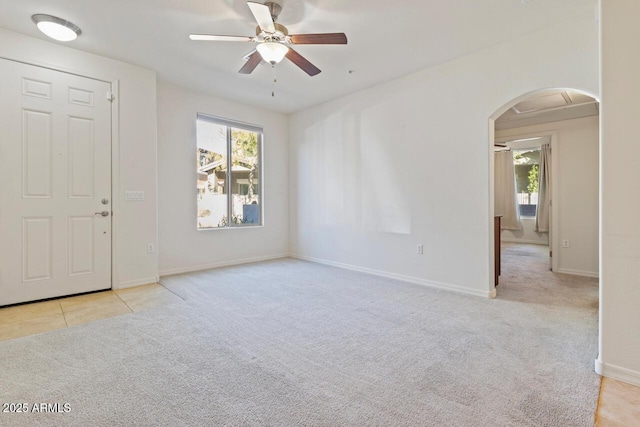 spare room featuring a wealth of natural light, arched walkways, light colored carpet, and a ceiling fan