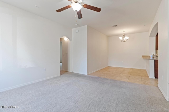 unfurnished room featuring visible vents, arched walkways, light colored carpet, ceiling fan with notable chandelier, and light tile patterned flooring