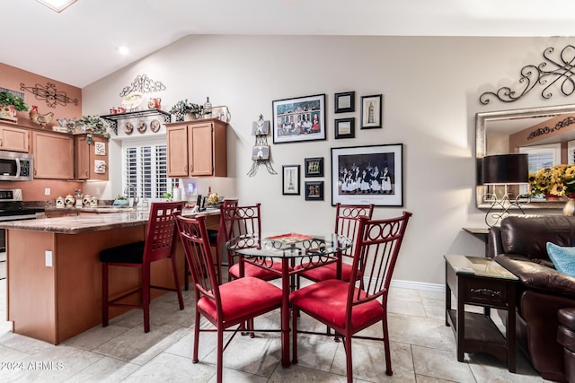 kitchen featuring light stone countertops, kitchen peninsula, stainless steel appliances, vaulted ceiling, and a breakfast bar area