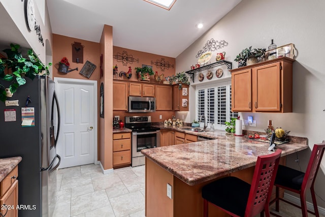 kitchen featuring stainless steel appliances, light stone counters, kitchen peninsula, vaulted ceiling, and a kitchen bar