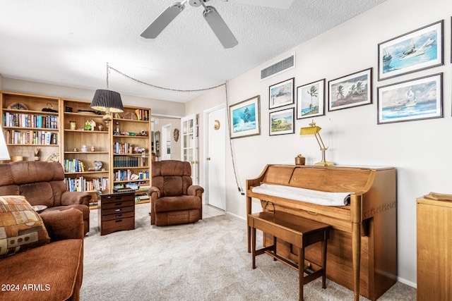 living area with ceiling fan, light colored carpet, and a textured ceiling