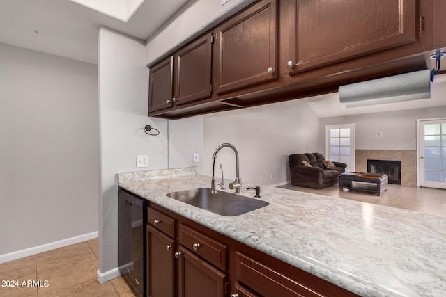 kitchen with a tile fireplace, dark brown cabinets, sink, light tile flooring, and dishwasher