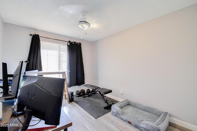 exercise area with ceiling fan, light hardwood / wood-style flooring, and a textured ceiling