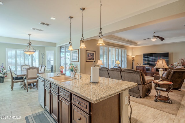 kitchen featuring light stone countertops, ceiling fan, sink, decorative light fixtures, and a center island with sink