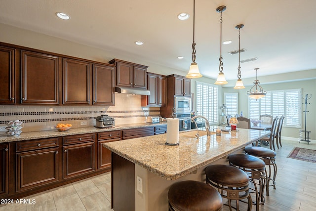 kitchen featuring pendant lighting, backsplash, an island with sink, and a breakfast bar area