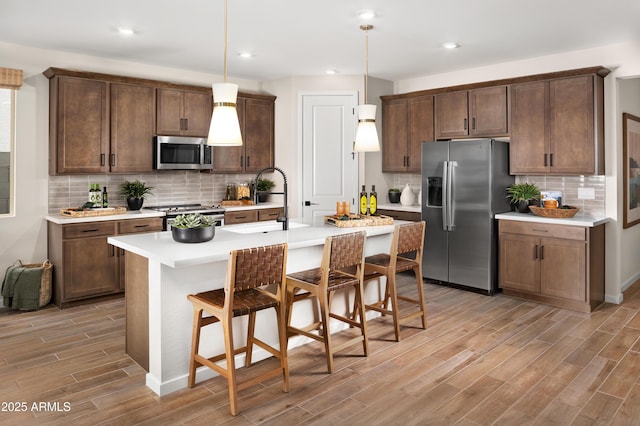 kitchen featuring stainless steel appliances, a kitchen breakfast bar, an island with sink, decorative light fixtures, and light wood-type flooring