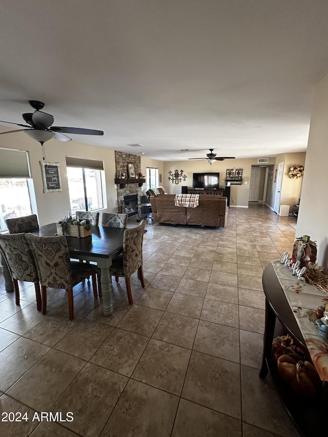 tiled dining area with a stone fireplace and ceiling fan