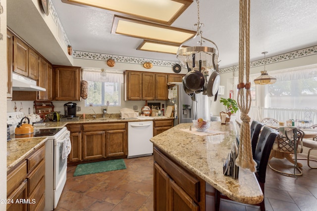 kitchen featuring white appliances, sink, hanging light fixtures, light stone countertops, and a textured ceiling