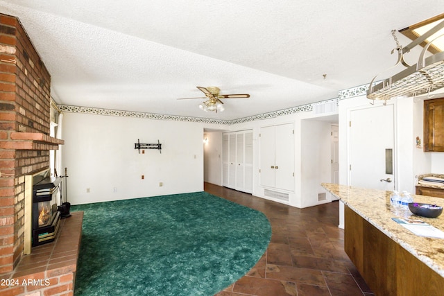 interior space featuring ceiling fan, a textured ceiling, and a brick fireplace