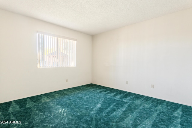 spare room featuring dark carpet and a textured ceiling