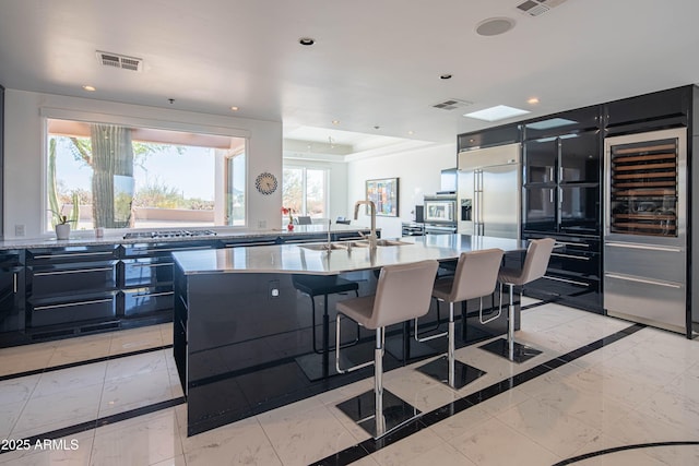 kitchen featuring sink, a breakfast bar, a kitchen island with sink, stainless steel appliances, and wine cooler