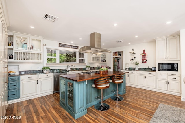 kitchen with island range hood, appliances with stainless steel finishes, visible vents, dark wood-style floors, and butcher block counters