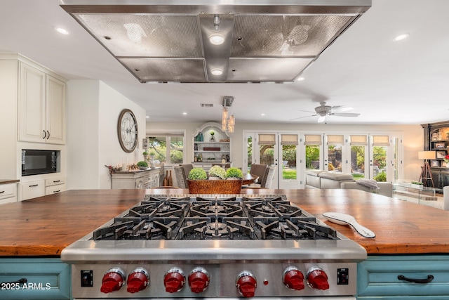 kitchen with wall chimney exhaust hood, wood counters, black microwave, high end stainless steel range oven, and open floor plan