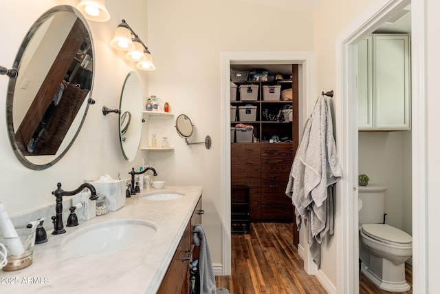 bathroom with toilet, double vanity, a sink, and wood finished floors