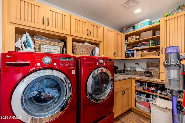 clothes washing area featuring a sink, washing machine and clothes dryer, cabinet space, light wood-style floors, and visible vents