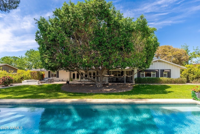 back of house with an outdoor pool, a yard, a patio, and board and batten siding