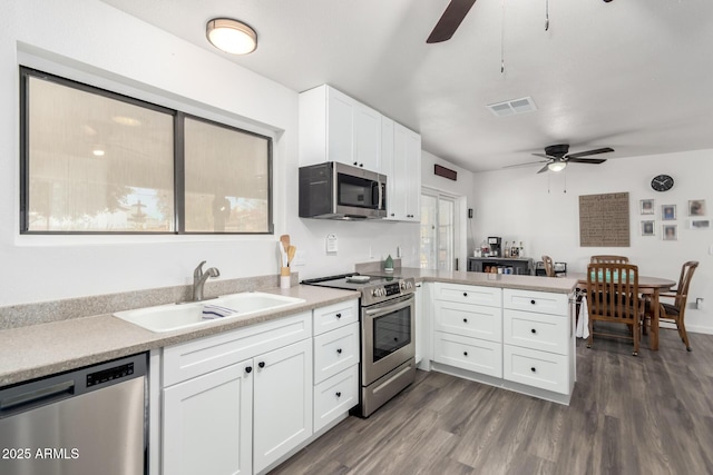 kitchen with appliances with stainless steel finishes, dark hardwood / wood-style floors, sink, white cabinets, and kitchen peninsula