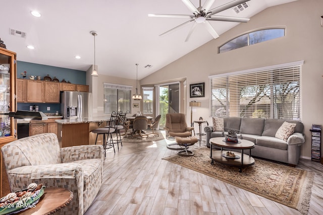 living room with high vaulted ceiling, light wood-type flooring, and ceiling fan with notable chandelier