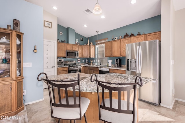 kitchen with hanging light fixtures, vaulted ceiling, a kitchen island, and appliances with stainless steel finishes