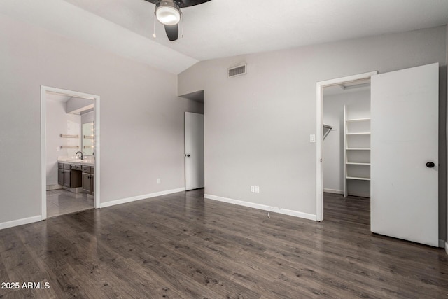 unfurnished bedroom featuring a walk in closet, dark wood finished floors, visible vents, vaulted ceiling, and a sink