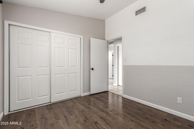 unfurnished bedroom with baseboards, a closet, visible vents, and dark wood-type flooring