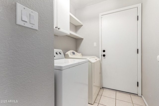 laundry area featuring cabinet space, a textured wall, washing machine and clothes dryer, and light tile patterned floors