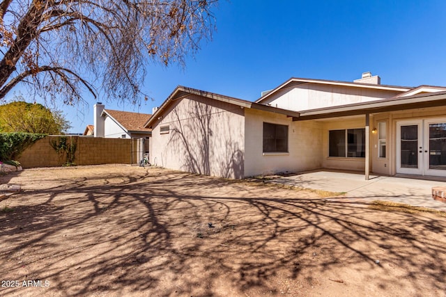 rear view of house with a patio, a chimney, concrete block siding, fence, and french doors