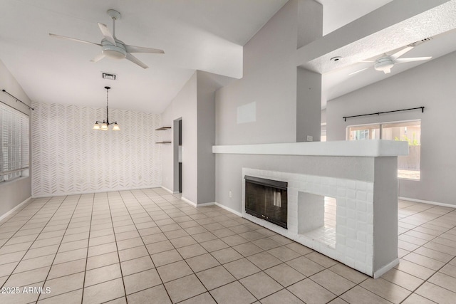 unfurnished living room with ceiling fan with notable chandelier, an accent wall, a fireplace, vaulted ceiling, and tile patterned floors