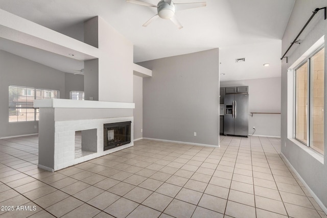 unfurnished living room featuring ceiling fan, light tile patterned floors, baseboards, vaulted ceiling, and a brick fireplace