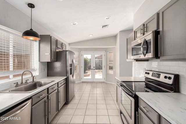 kitchen featuring gray cabinets, appliances with stainless steel finishes, light tile patterned flooring, a sink, and vaulted ceiling