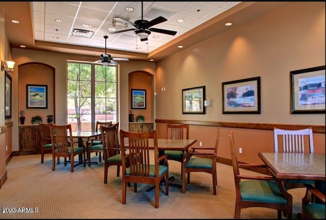 dining space with ceiling fan, a tray ceiling, and light colored carpet