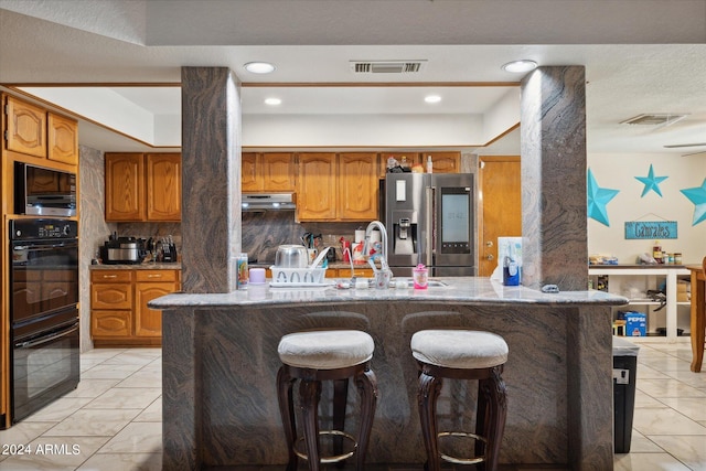 kitchen with a kitchen bar, kitchen peninsula, decorative backsplash, stainless steel fridge with ice dispenser, and a raised ceiling