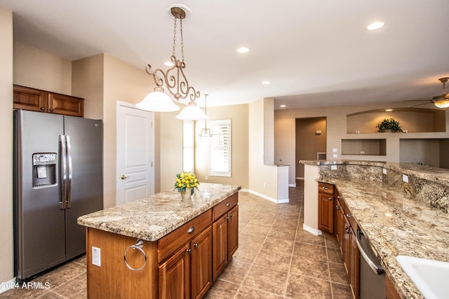 kitchen with light stone counters, a center island, hanging light fixtures, ceiling fan, and appliances with stainless steel finishes