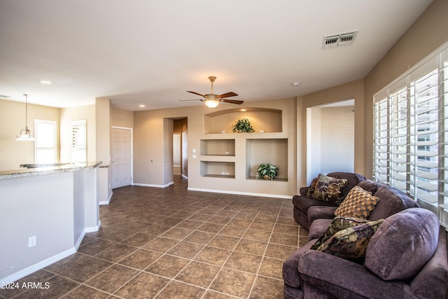 living room with built in shelves, dark tile patterned flooring, and ceiling fan