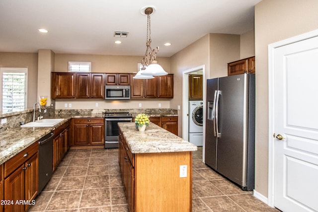 kitchen with a kitchen island, appliances with stainless steel finishes, washer / clothes dryer, pendant lighting, and sink