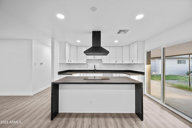 kitchen with a kitchen island with sink, white cabinets, sink, light hardwood / wood-style floors, and island exhaust hood