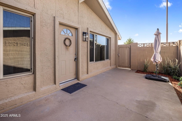 entrance to property featuring stucco siding, a patio, and fence