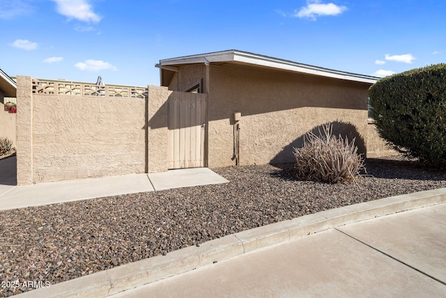 view of side of property featuring stucco siding, fence, and a gate