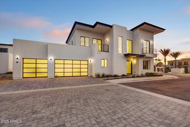 view of front of home featuring decorative driveway, a balcony, an attached garage, and stucco siding