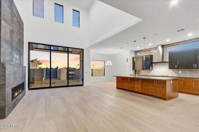 kitchen featuring light wood-type flooring, a fireplace, decorative backsplash, wall chimney exhaust hood, and open floor plan