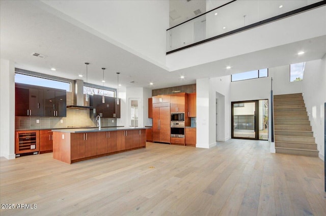 kitchen featuring visible vents, wine cooler, open floor plan, built in appliances, and wall chimney exhaust hood