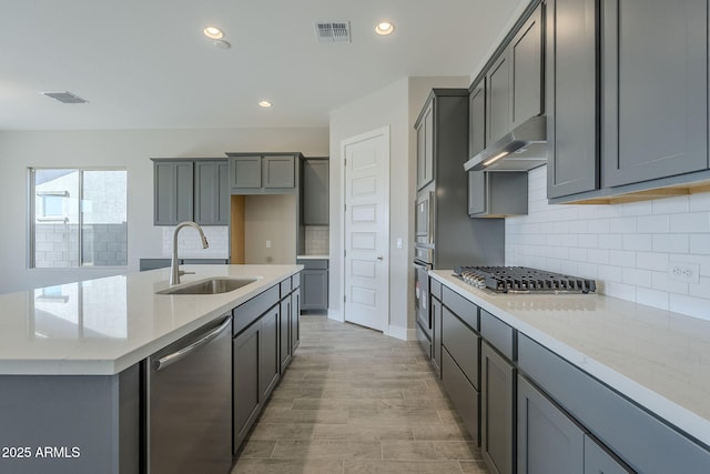 kitchen featuring gray cabinets, appliances with stainless steel finishes, sink, a center island with sink, and light wood-type flooring