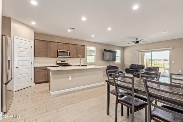 kitchen with light hardwood / wood-style floors, sink, a kitchen island with sink, ceiling fan, and appliances with stainless steel finishes