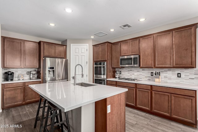 kitchen with sink, light hardwood / wood-style flooring, appliances with stainless steel finishes, a kitchen island with sink, and a kitchen breakfast bar