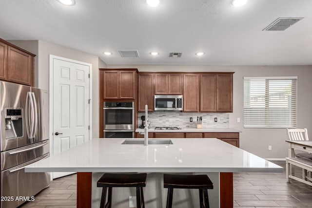 kitchen featuring sink, appliances with stainless steel finishes, a kitchen breakfast bar, a center island with sink, and decorative backsplash