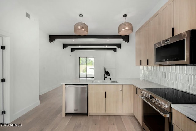 kitchen featuring decorative light fixtures, a peninsula, stainless steel appliances, light brown cabinetry, and a sink